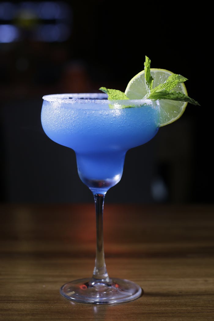 Servicios A vibrant blue margarita cocktail with lime and mint garnish on a wooden table.