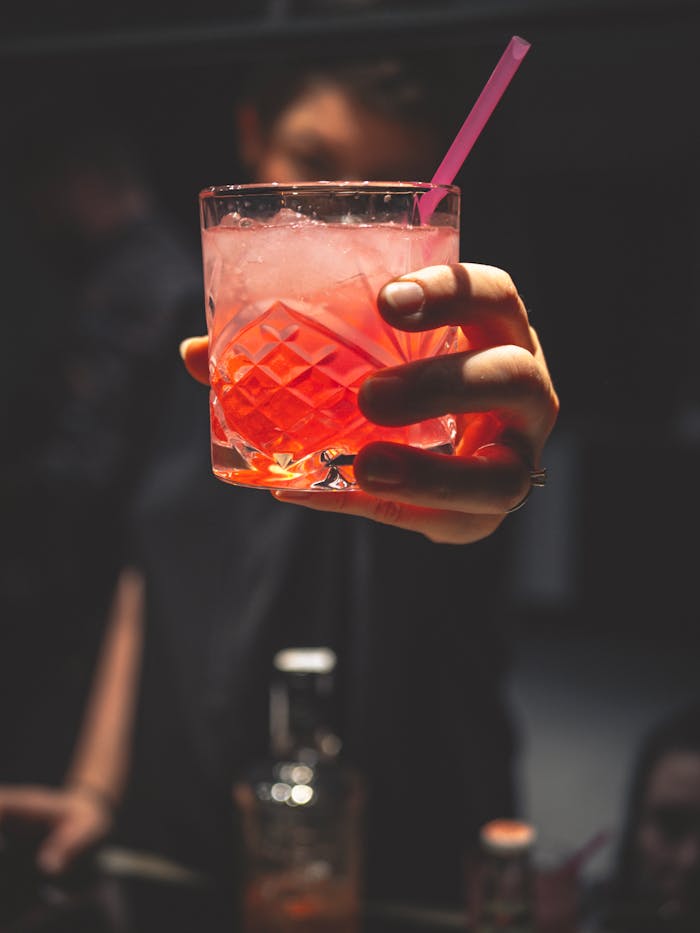 Acerca de Close-up of a hand holding a vibrant cocktail with ice and a straw, perfect for nightlife themes.