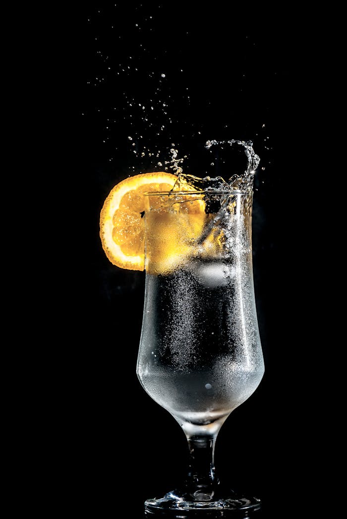 Servicios Dazzling cold cocktail with citrus slice splash, set against a dramatic black background.